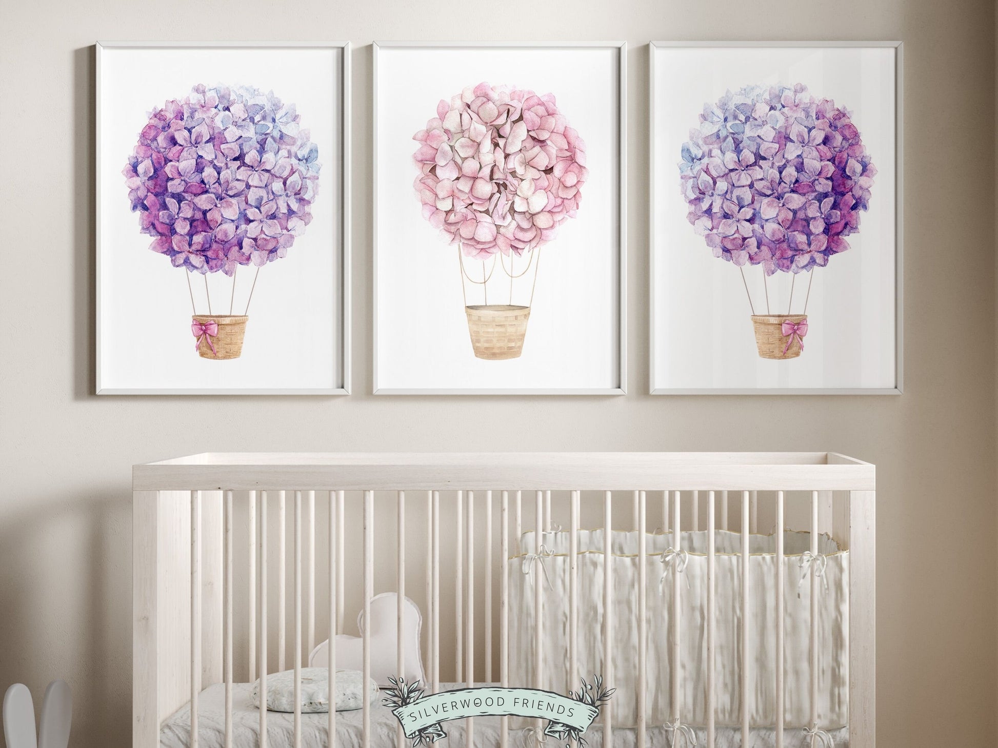 Set of 3 watercolor Hot Air Balloon Prints featuring delightful pink and purple wildflower adorned balloons. A charming addition to your nursery decor and makes an adorable baby shower gift, these prints infuse sweetness and elegance into any space.