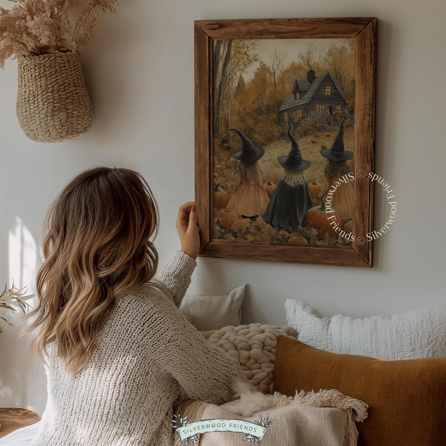Cozy Halloween poster for downstairs — painterly cottage landscape with three figures in cloaks, glowing windows, and rustic autumn surroundings